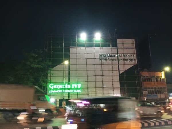 Illuminated building signage on a scaffolded facade at night beside a busy main road in Chennai